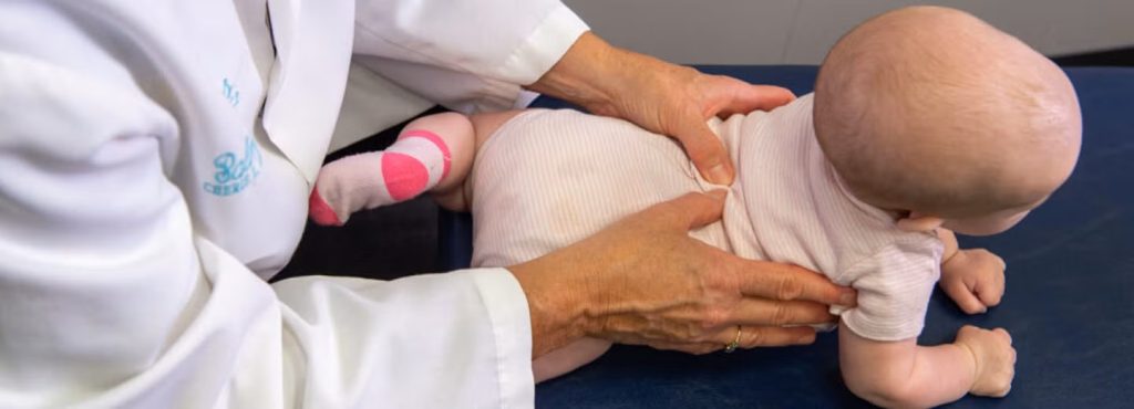 Gentle paediatric chiropractic assessment being performed on a baby during tummy time, with a chiropractor using light hands-on techniques to assess spinal and postural movement.