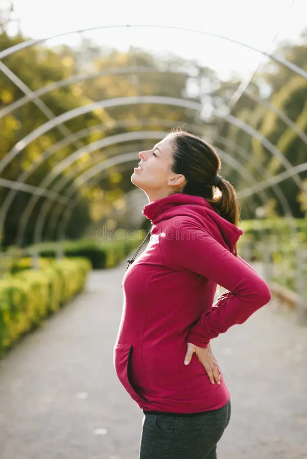 Pregnant woman experiencing lower back and sciatic nerve discomfort while gently holding her lower back, representing sciatica during pregnancy and the physical changes that occur throughout pregnancy.