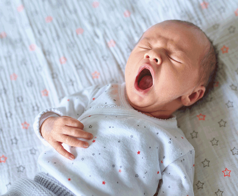 Newborn baby lying on a blanket with eyes closed and mouth open, representing common signs that may lead parents to seek a developmental or chiropractic assessment.