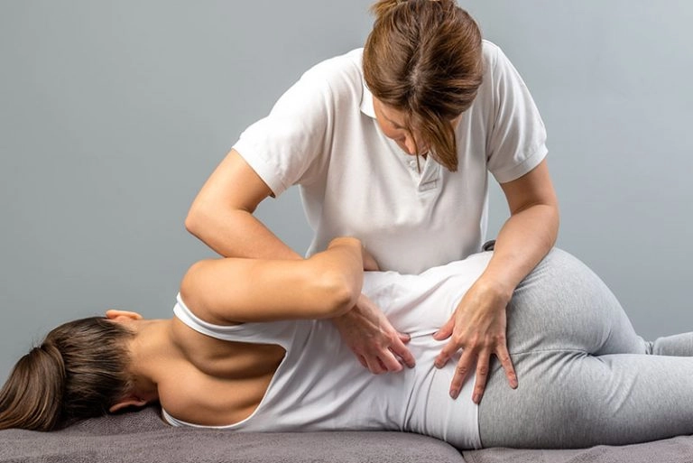 Chiropractor assessing a patient's lower back and hip during an examination for chronic pain potentially related to previous injuries and compensation patterns.