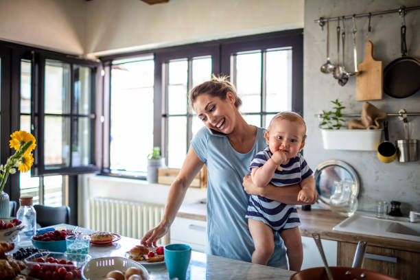 Busy mother holding her baby while preparing food in the kitchen, illustrating how parents often prioritise everyone else's needs before their own health.